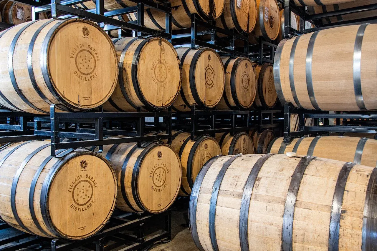 Racked oak barrels aging whiskey inside Village Garage Distillery
