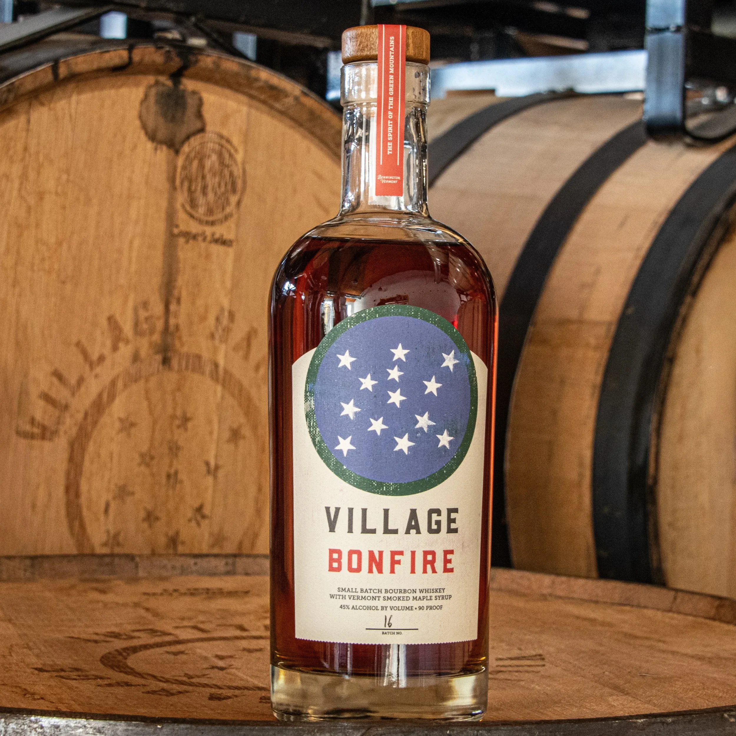 Bottle of Village Bonfire smoked maple bourbon in front of charred oak barrels