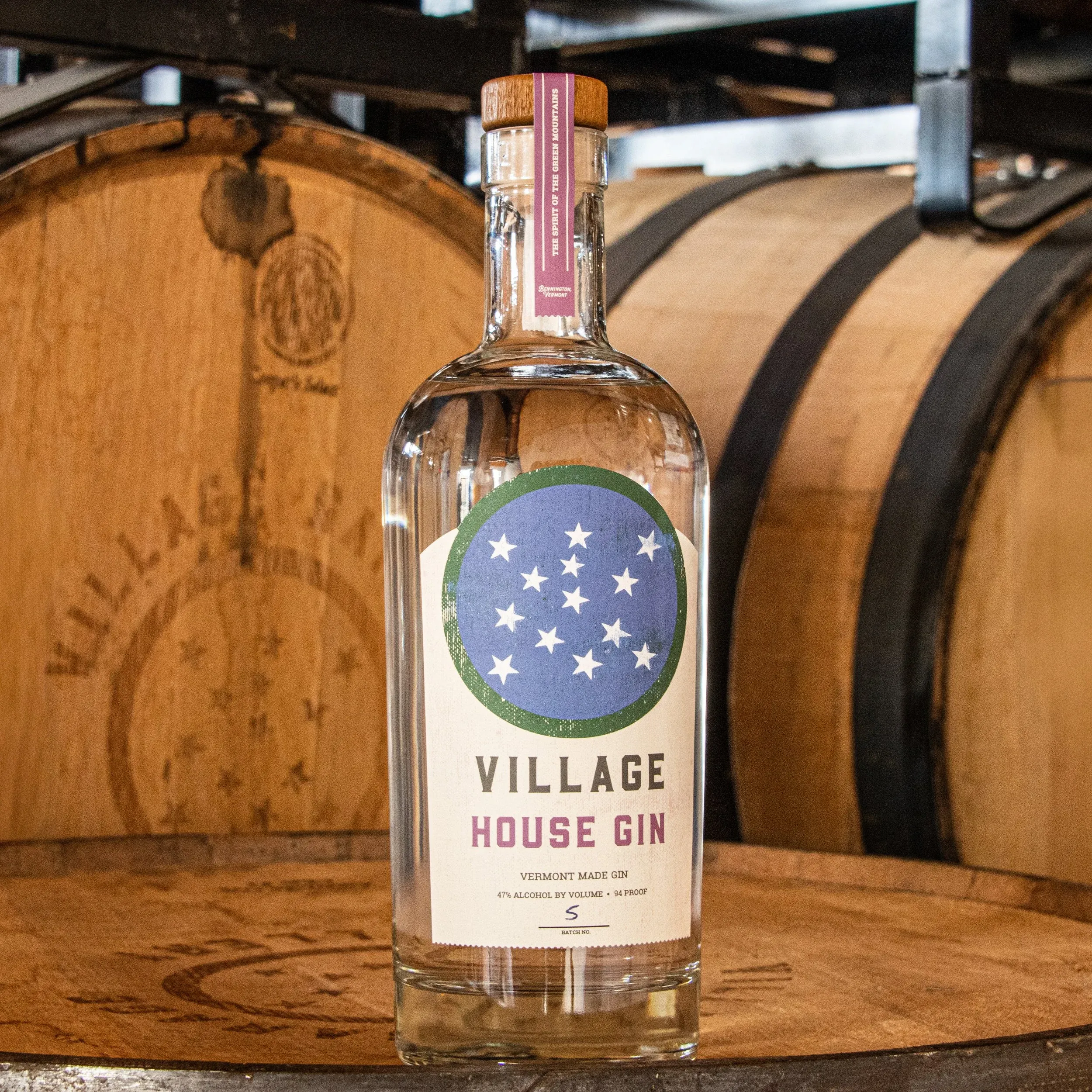 Bottle of Village House Gin in front of oak barrels