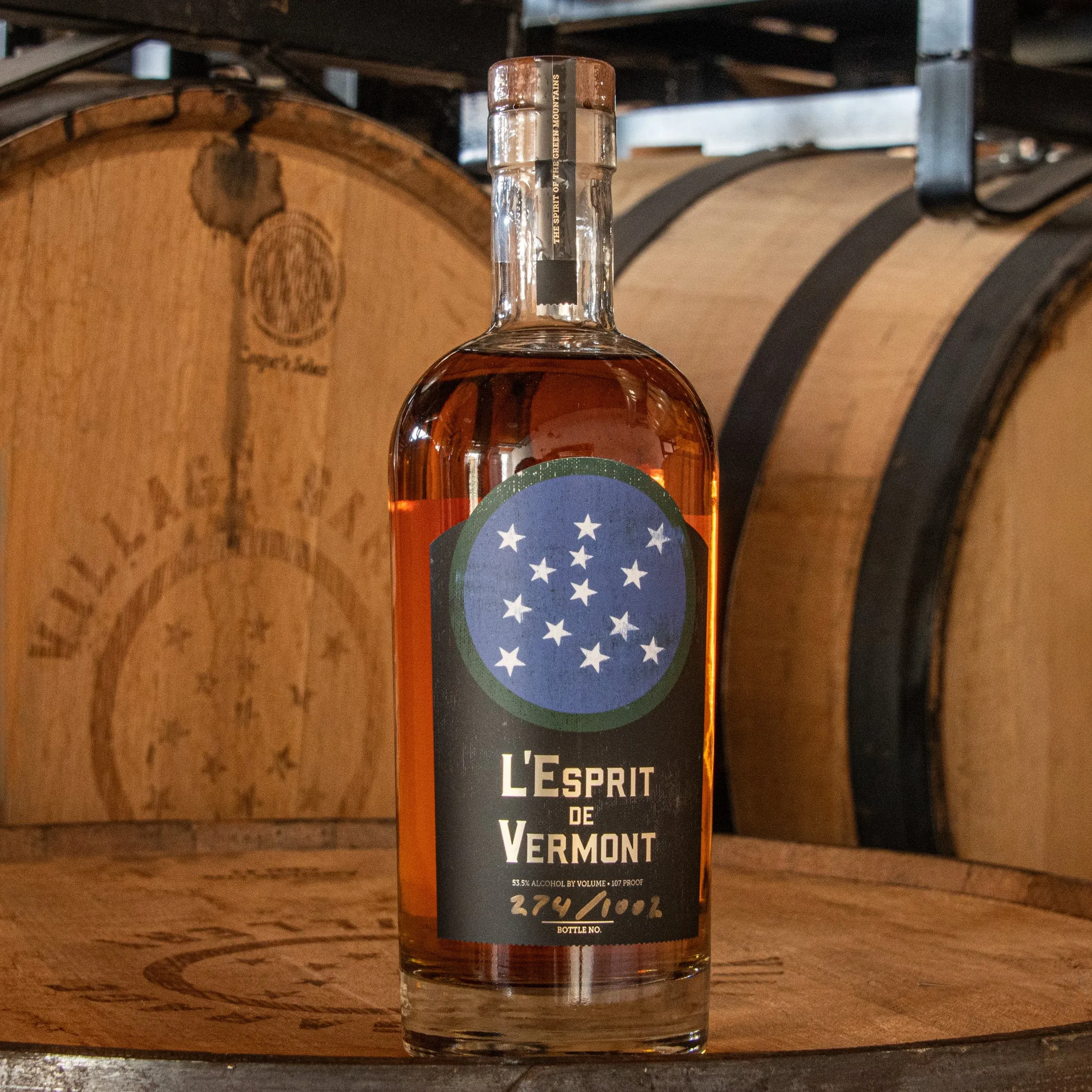 Bottle of L'Esprit de Vermont Armagnac cask-finished whiskey in front of oak barrels