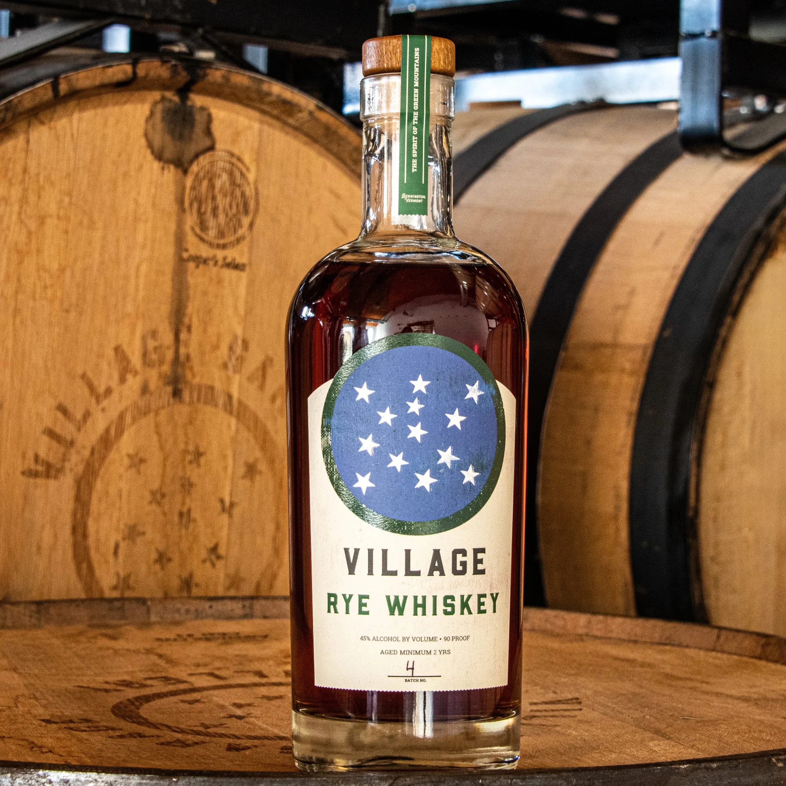 Bottle of Village Rye whiskey in front of oak barrels