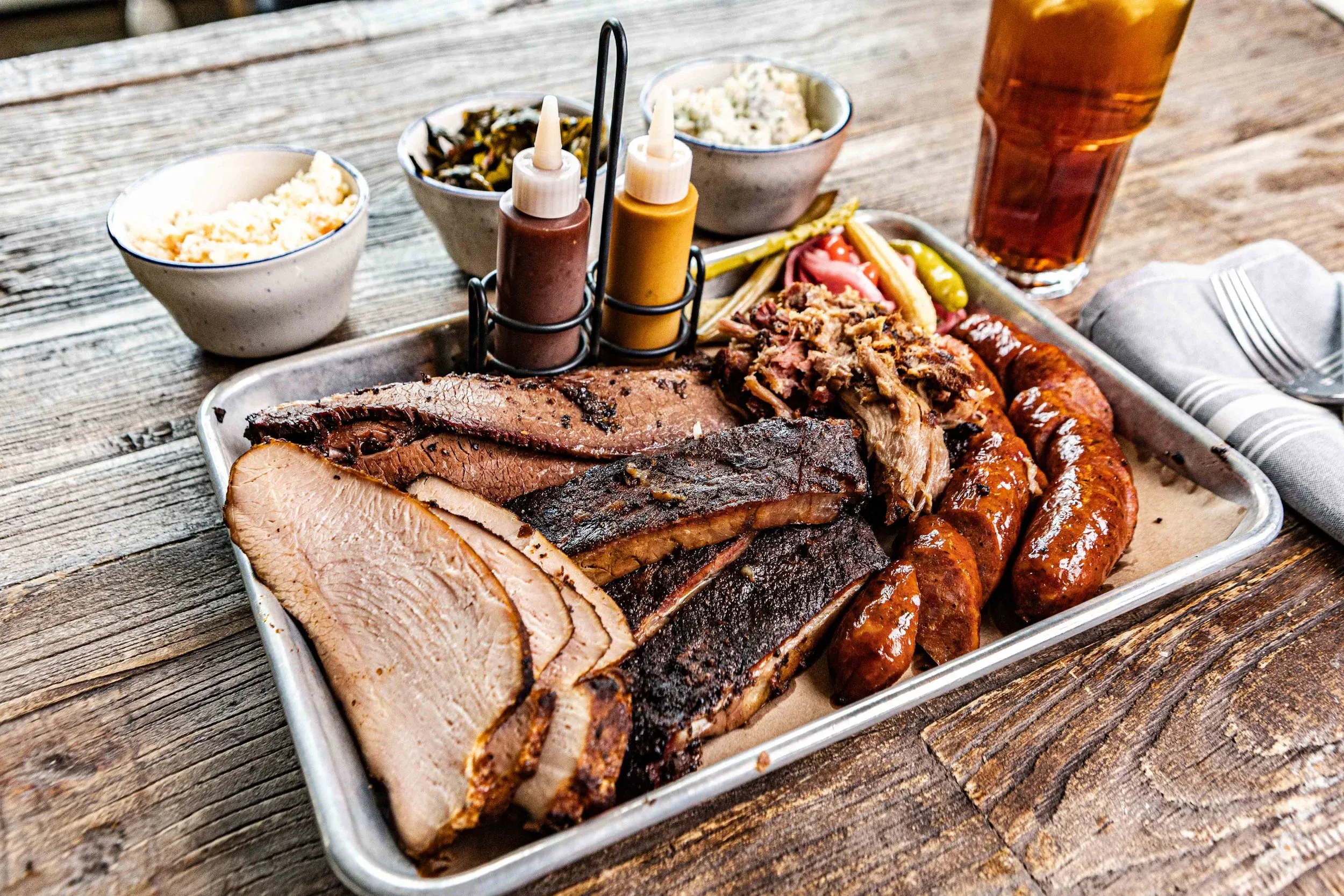 A tray of barbecue meats with sides, including brisket, pulled pork, and sausage, at Pearl's at the Garage